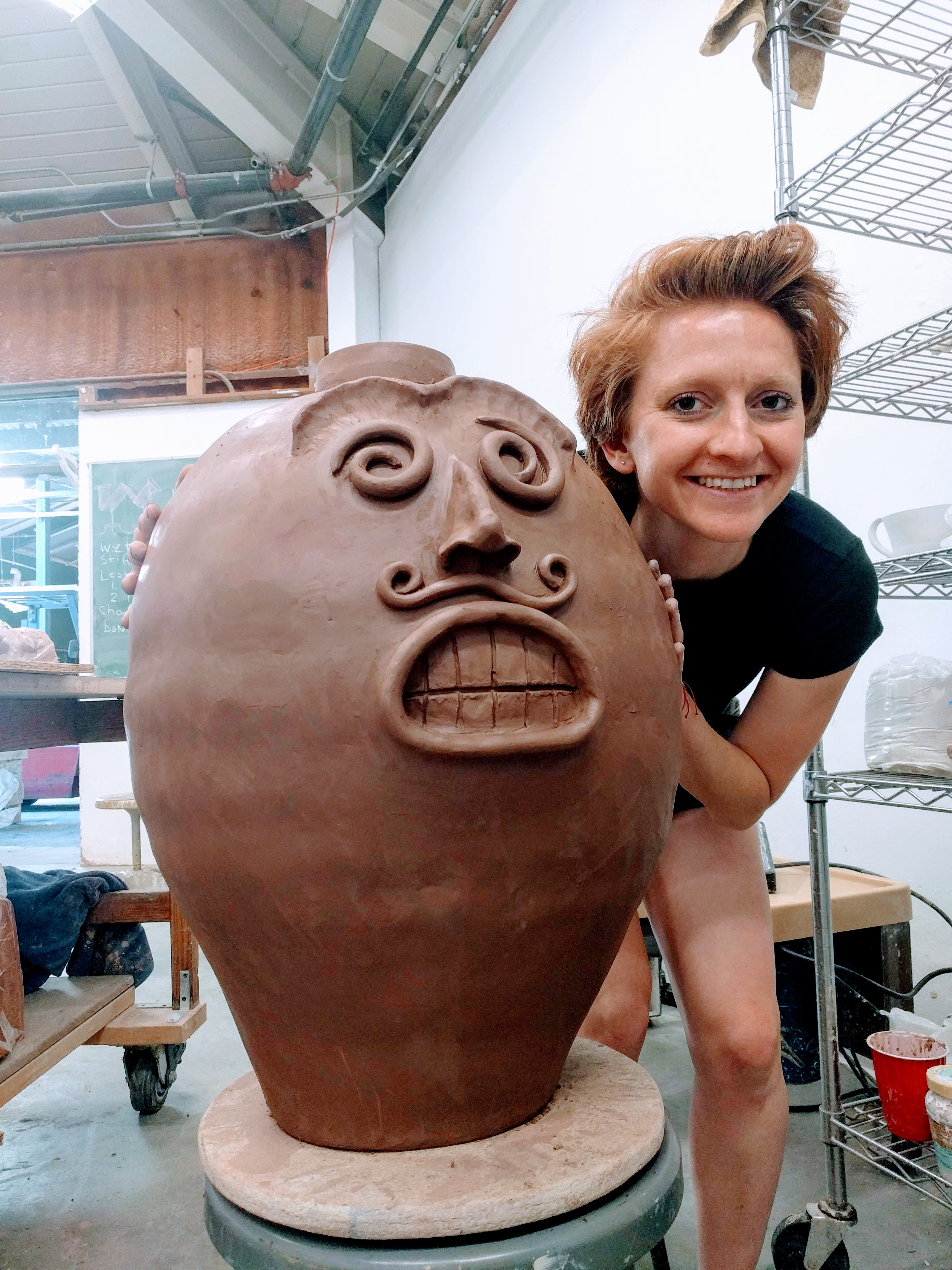 Aisha crouching next to a big ceramic pot she made.