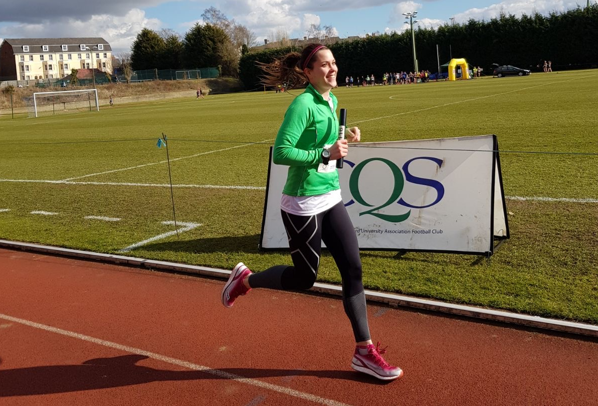 Young happy woman running along track.