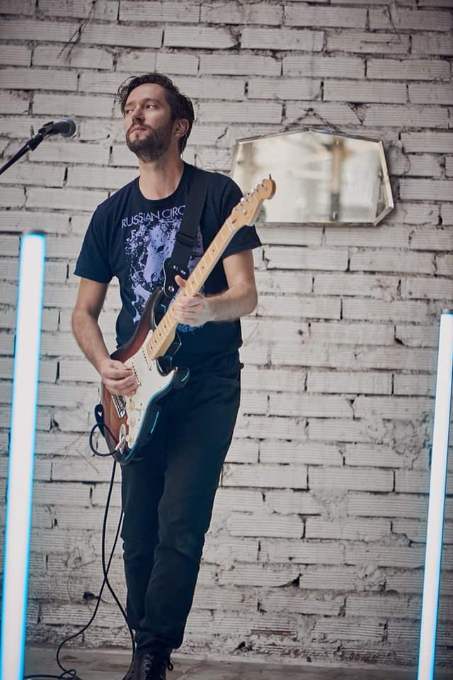 Young man playing bass guitar in front of a white distressed brick background.